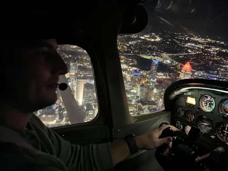 Cockpit view at night, pilot flying over a brightly lit city with instrument panel visible