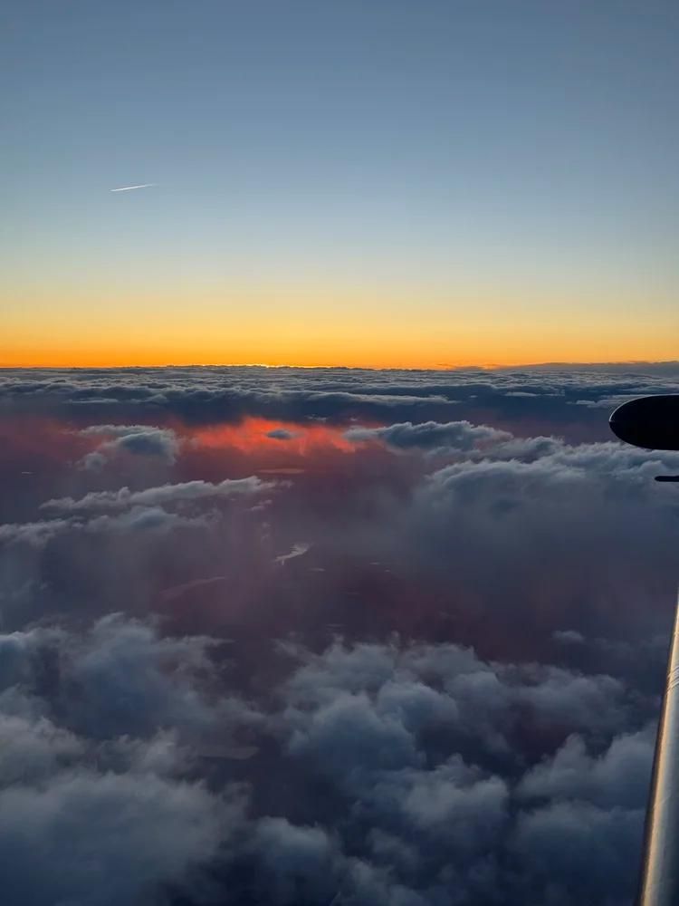Sunset above a sea of clouds, with orange horizon and blue sky seen from an airplane window