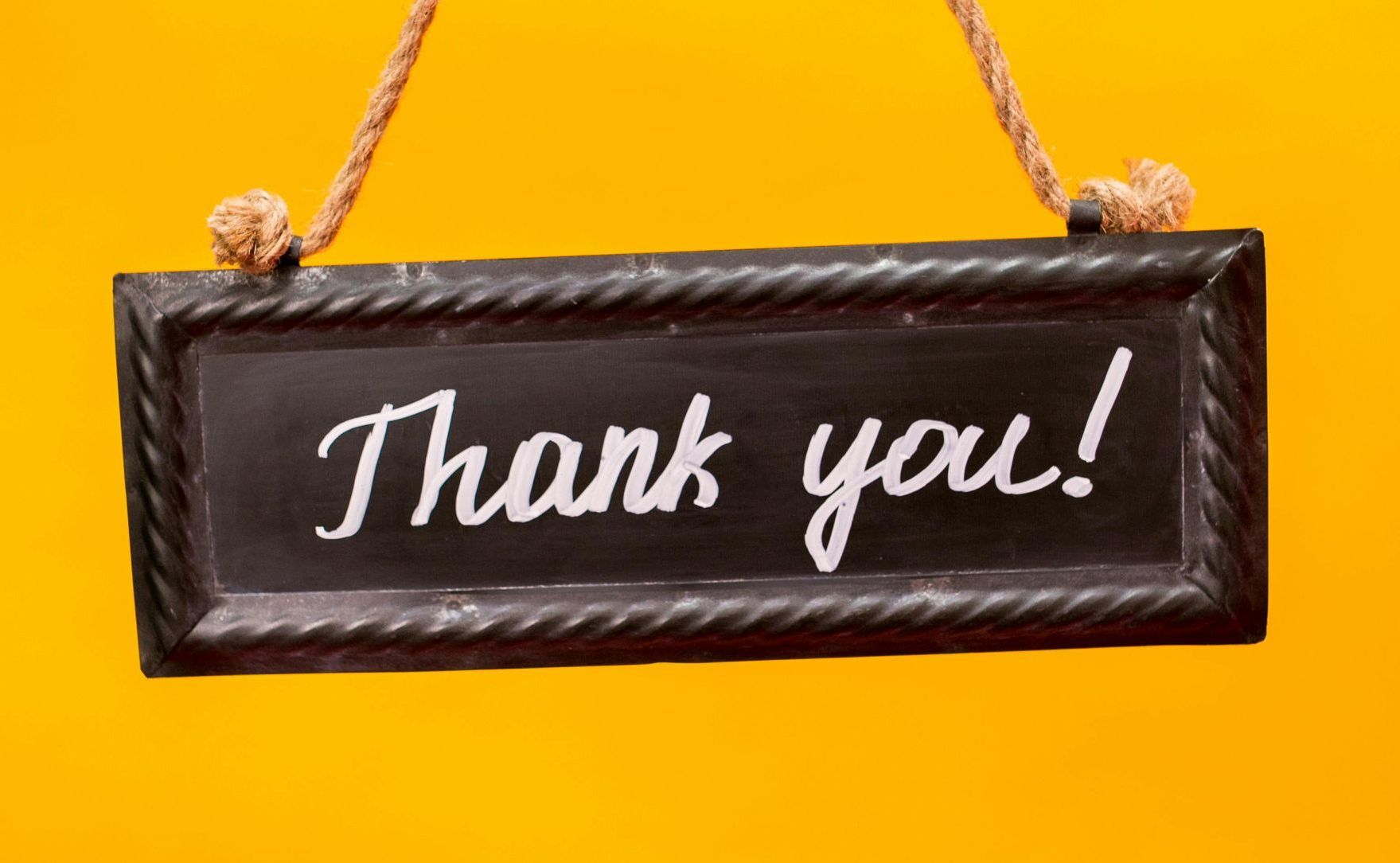 A blackboard with the words `` thank you '' written on it is hanging on a yellow wall.