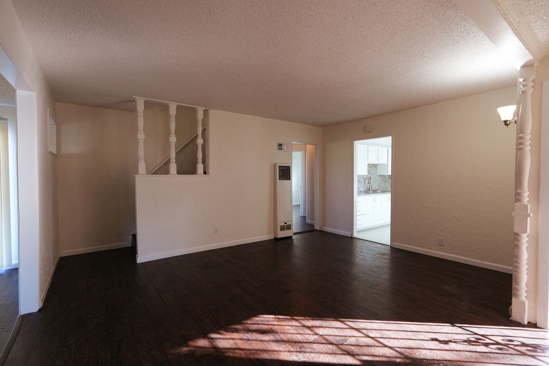 West Covina  Empty living room with beige walls, dark wood floors, and sunlight streaming through a window.