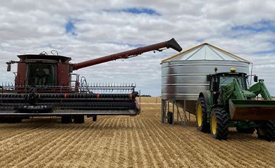 A combine harvester is loading grain into a silo next to a tractor.