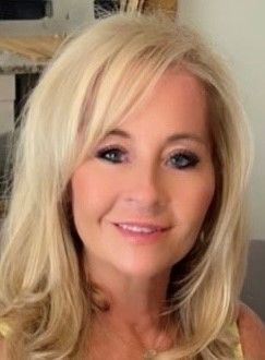 A woman with blonde hair and a necklace is smiling for the camera.