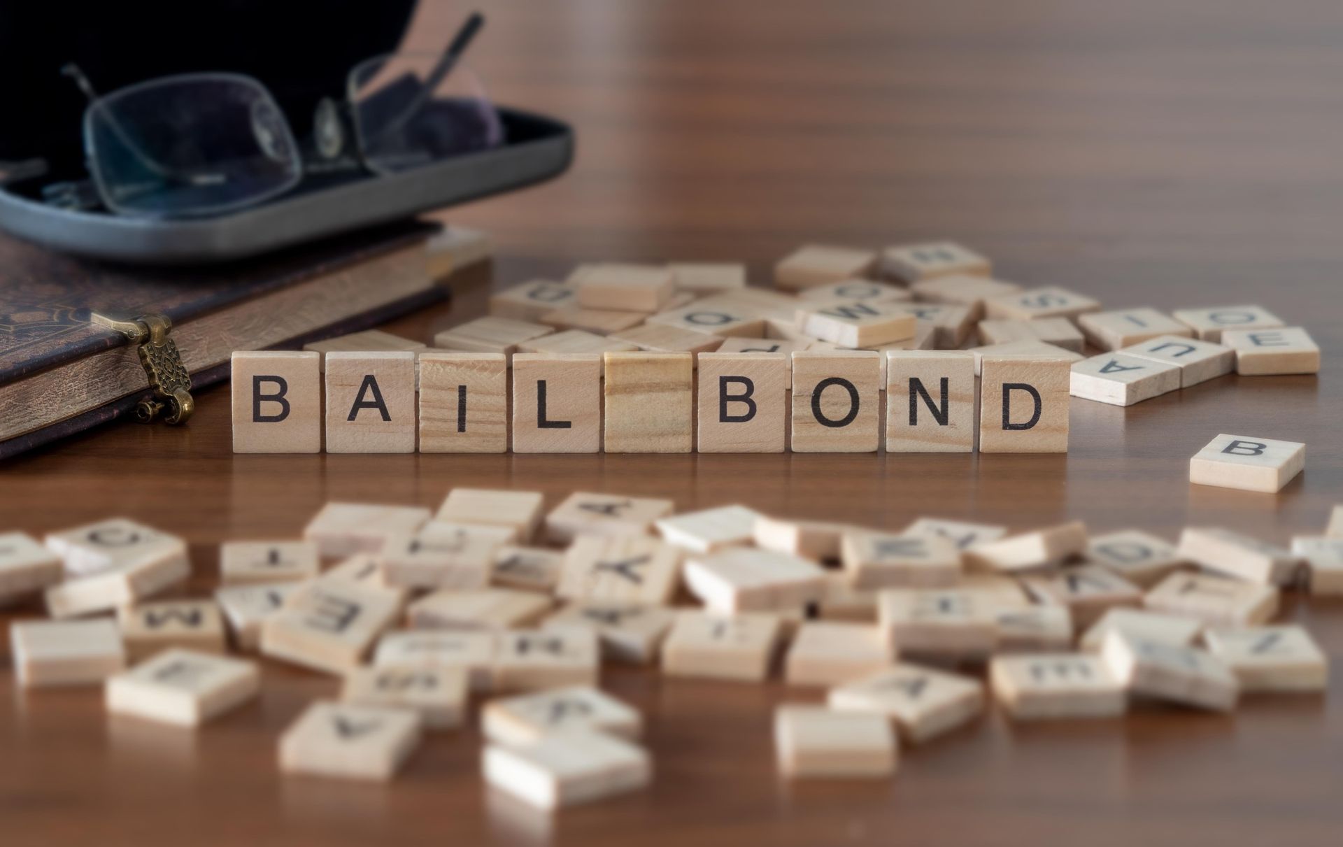 Wooden letter tiles spell out “Bail Bond” on a table beside scattered game pieces.