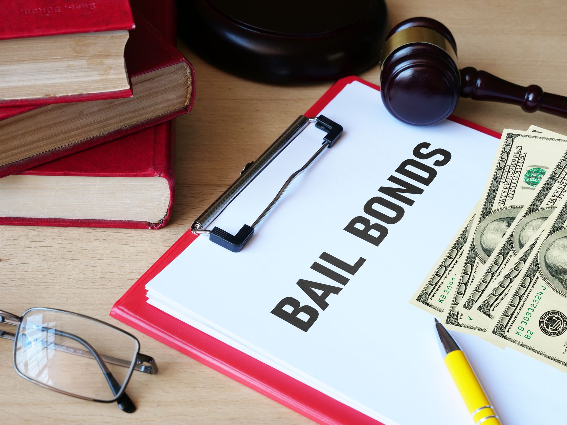 Bail bonds paperwork with a gavel, cash, glasses, and law books on a desk.