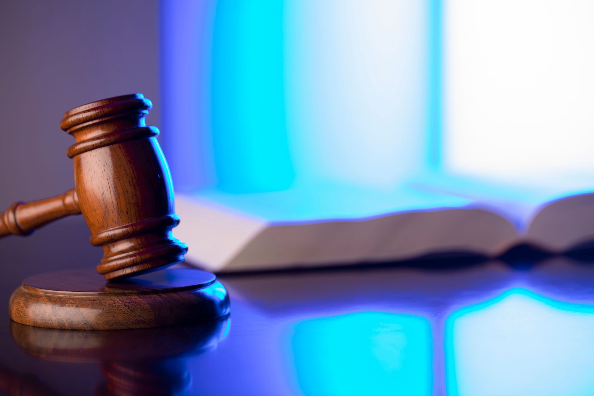 Wooden gavel on a stand, with a partially open book in a blue-lit setting.