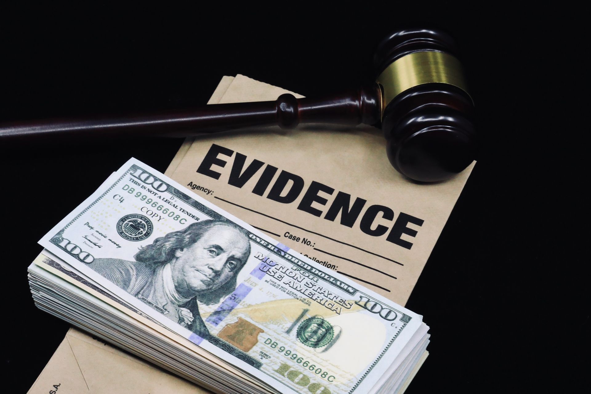 A gavel, evidence envelope, and stack of hundred-dollar bills on a black background
