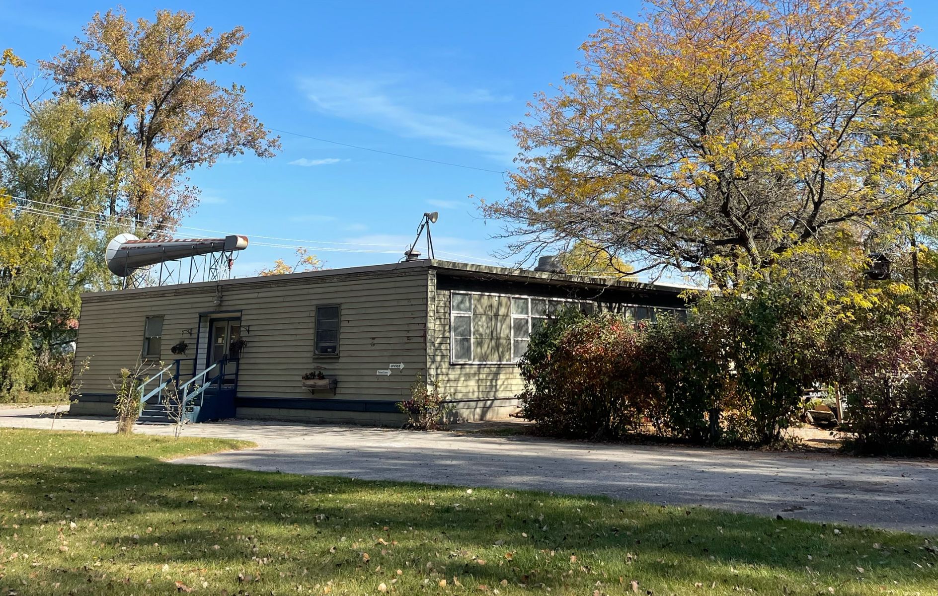 A single-story building under a bright blue sky, surrounded by trees with fall foliage.