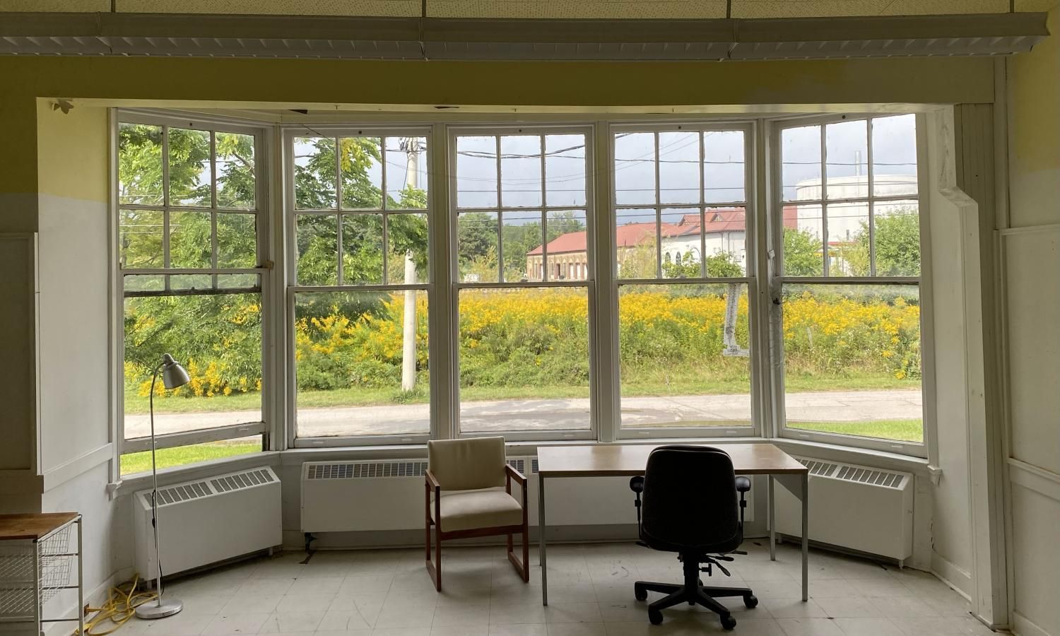 Interior view of room with a large bay window overlooking a field. Office furniture inside.