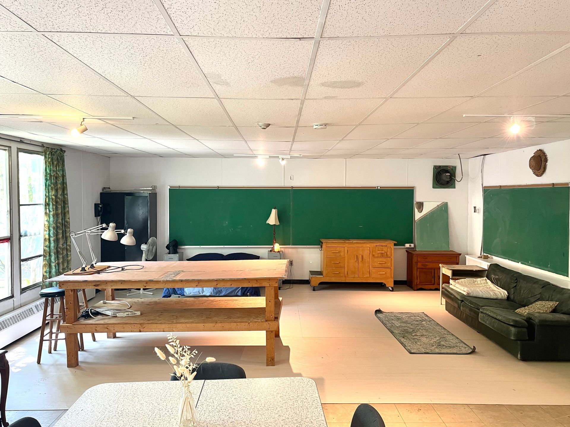 Art studio with green chalkboard, wooden table, couch, and natural light.