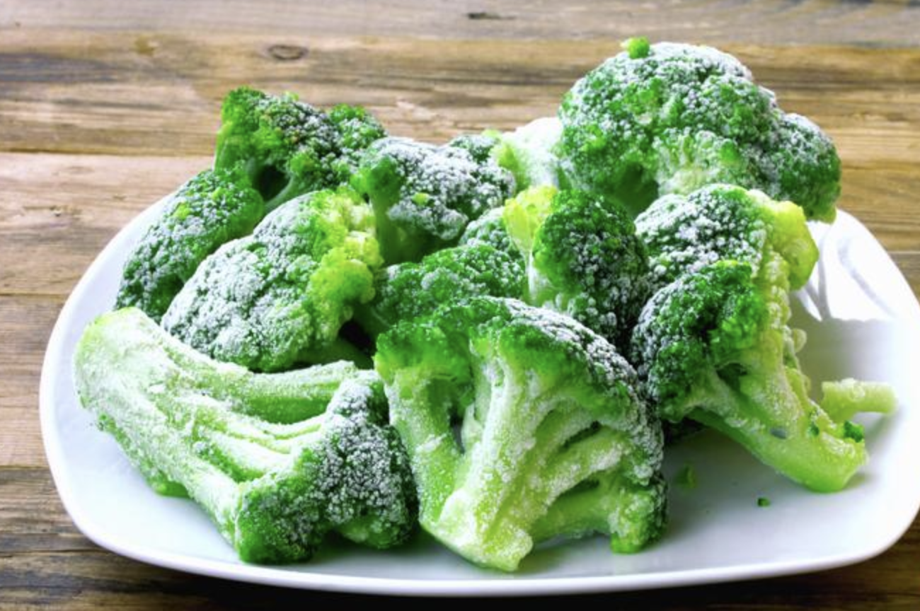 Un plato blanco cubierto con brócoli congelado sobre una mesa de madera.