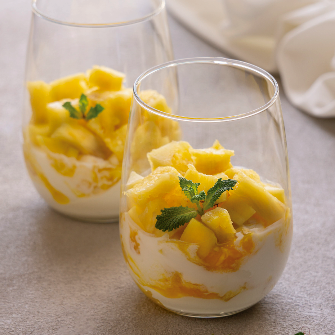 Dos vasos llenos de piña y yogur sobre una mesa.