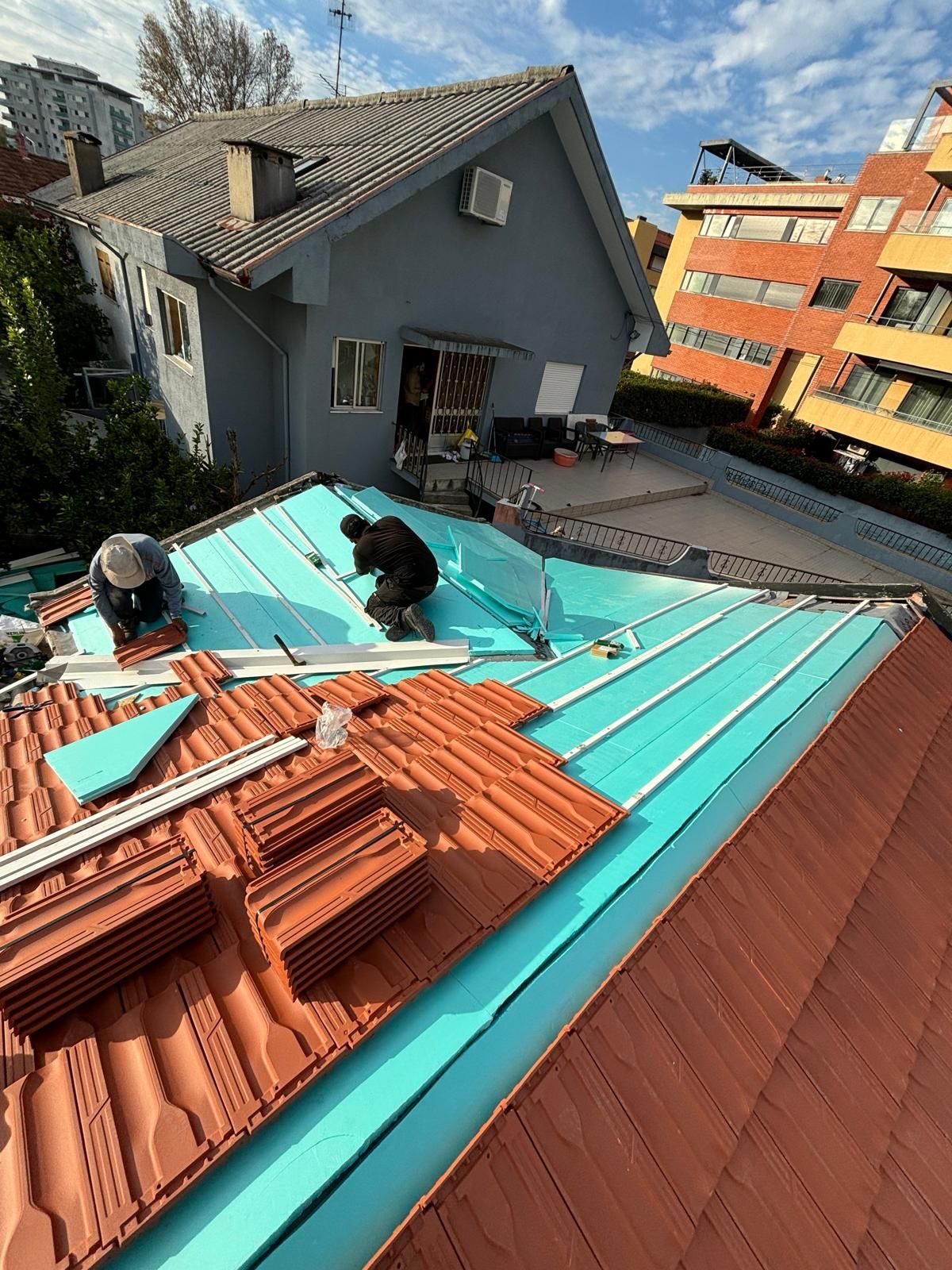 Dois homens estão trabalhando no telhado de uma casa com telhas cerâmicas marselha.