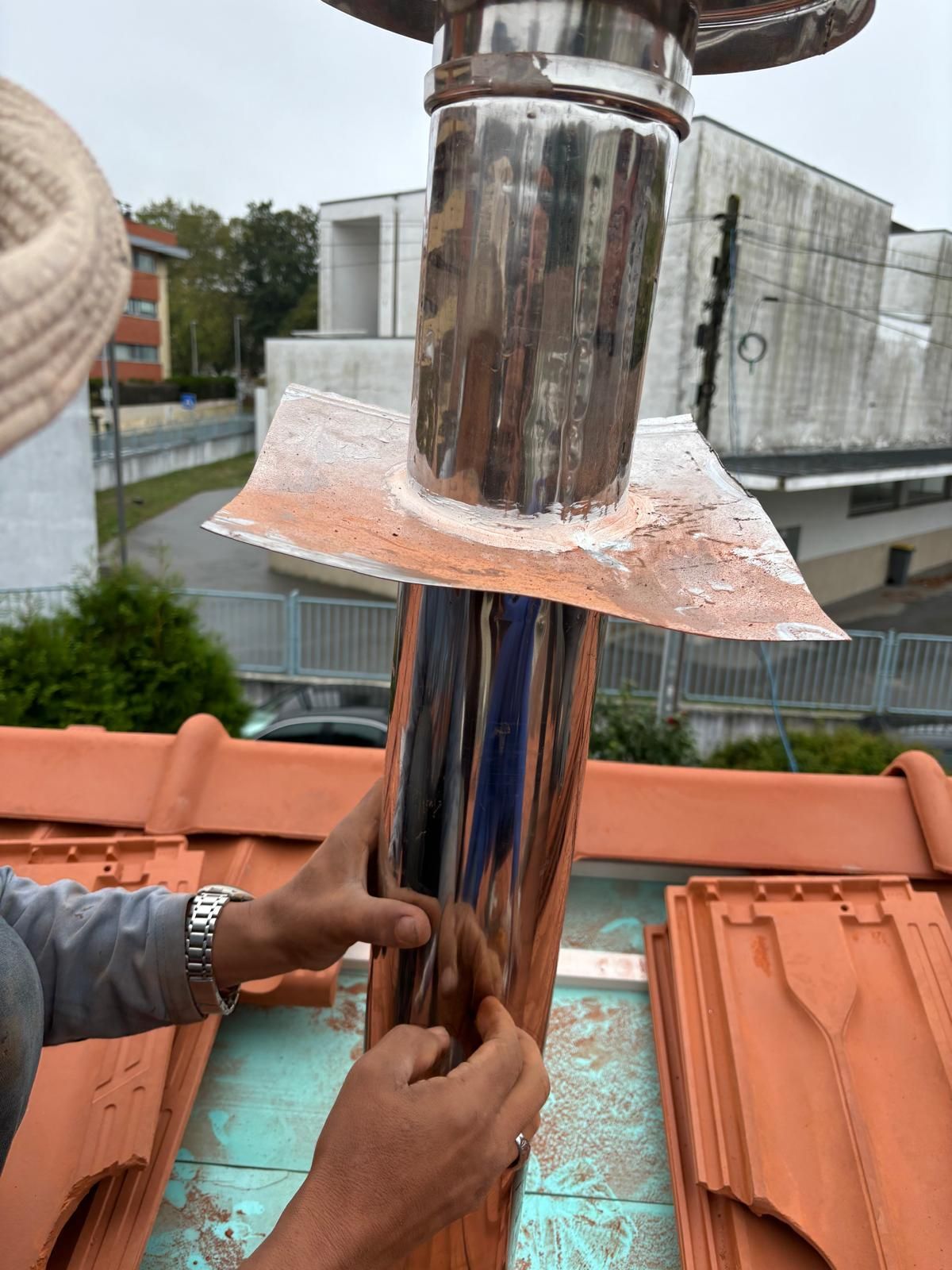 Um homem está trabalhando em uma chaminé no telhado de telhas cerâmicas marselha..