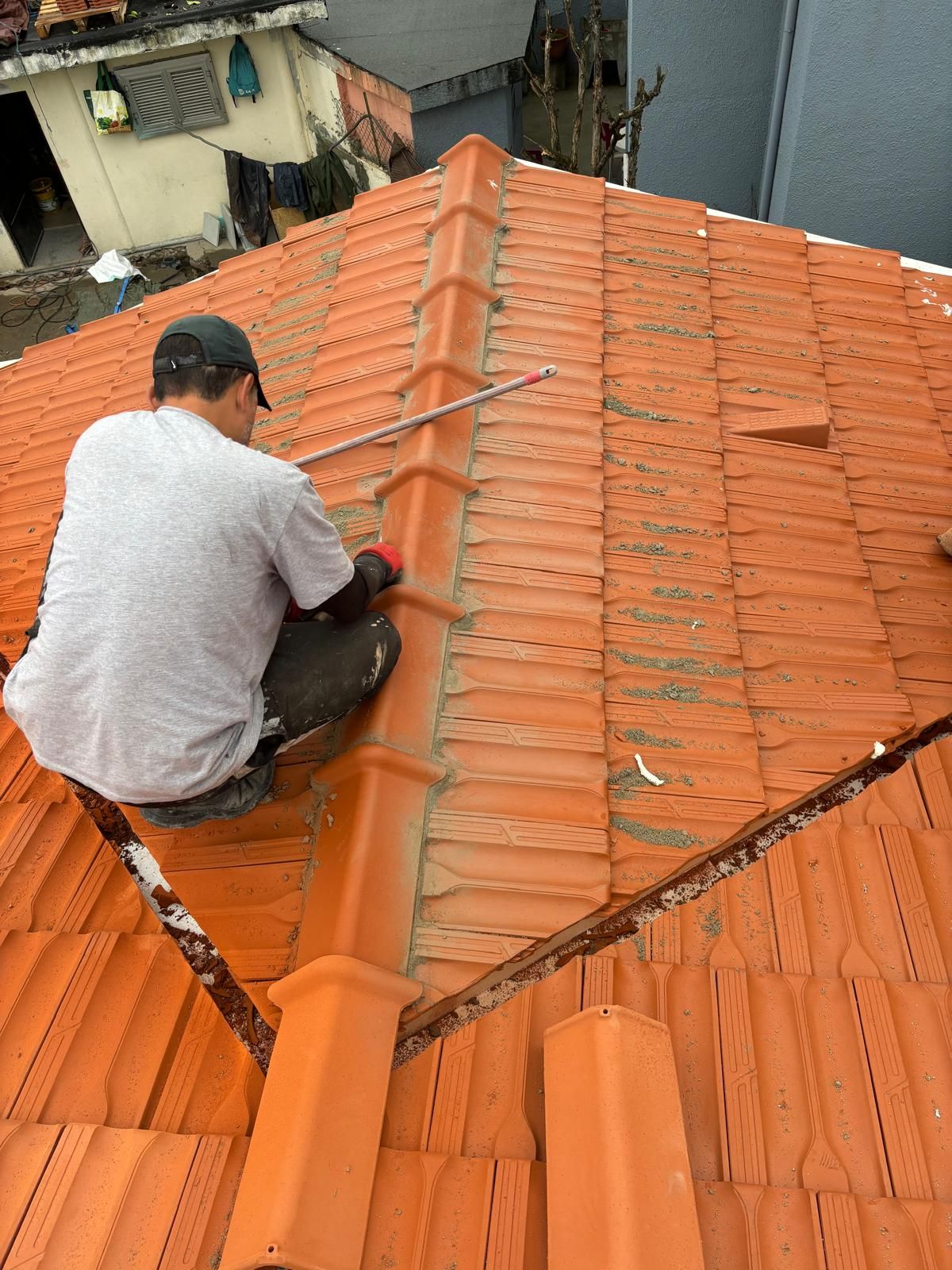 Um homem está sentado no topo de um telhado de telhas cerâmicas marselha.