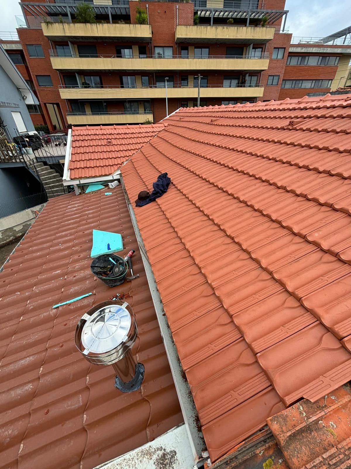 Um telhado de telhas cerâmicas laranjas  com um edifício ao fundo.