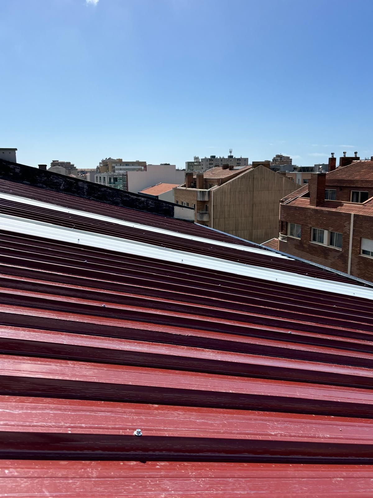 O telhado de um prédio com um telhado vermelho e um céu azul ao fundo.