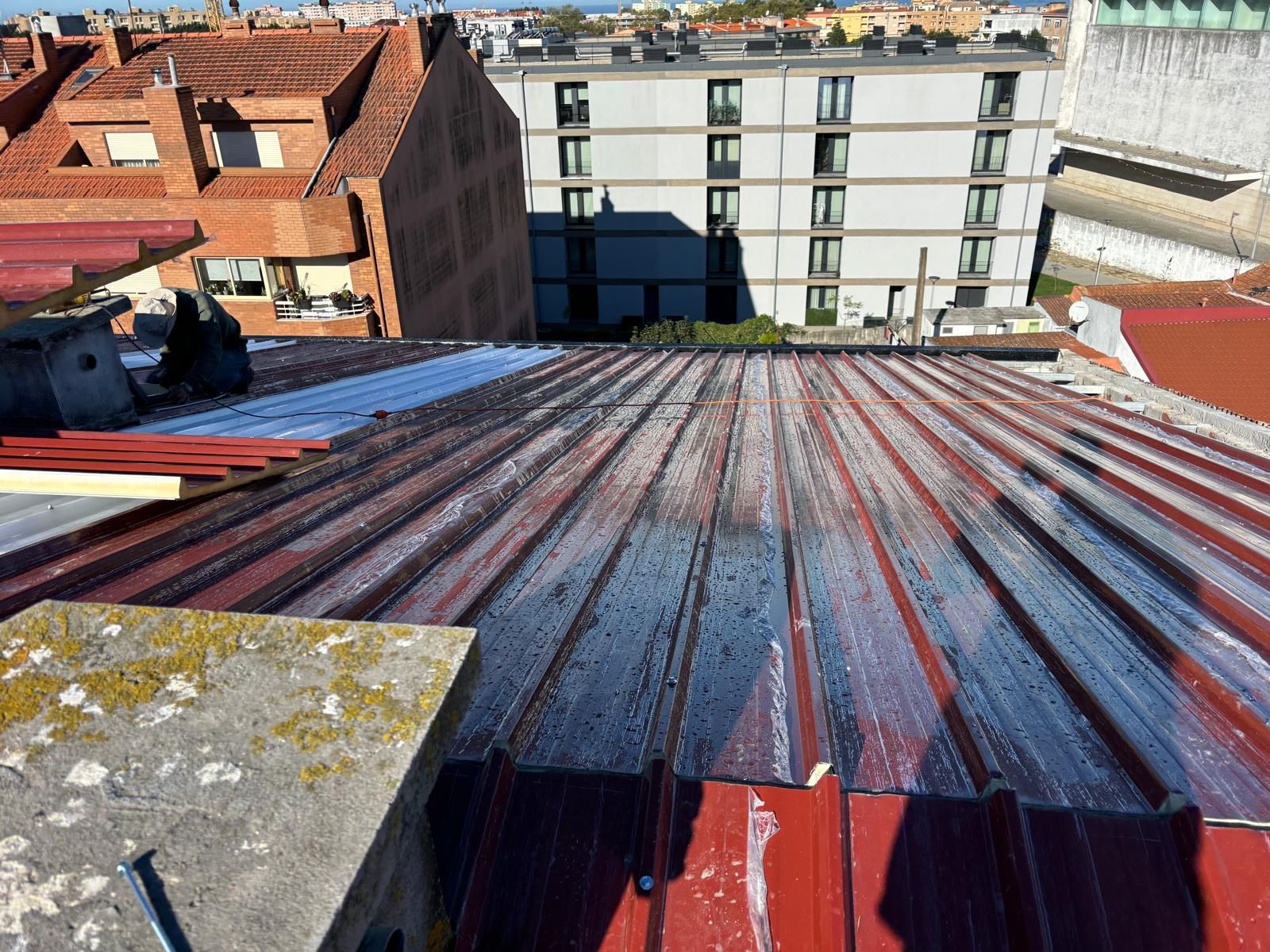 Um telhado em painel sandwich 5 ondas 30mmde metal enferrujado com um prédio ao fundo