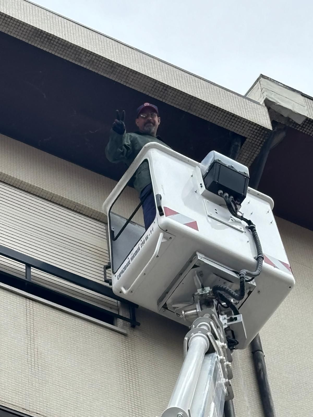 Um homem está de pé dentro de uma Grua usada para pintar os tubos de queda de um prédio