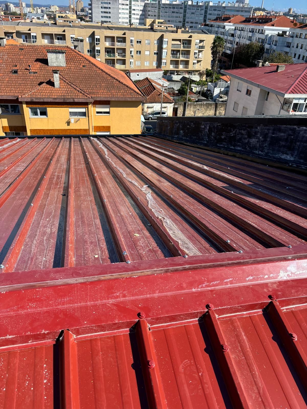 Um telhado vermelho em painel sandwich 5 ondas 30mmcom um prédio amarelo ao fundo.
