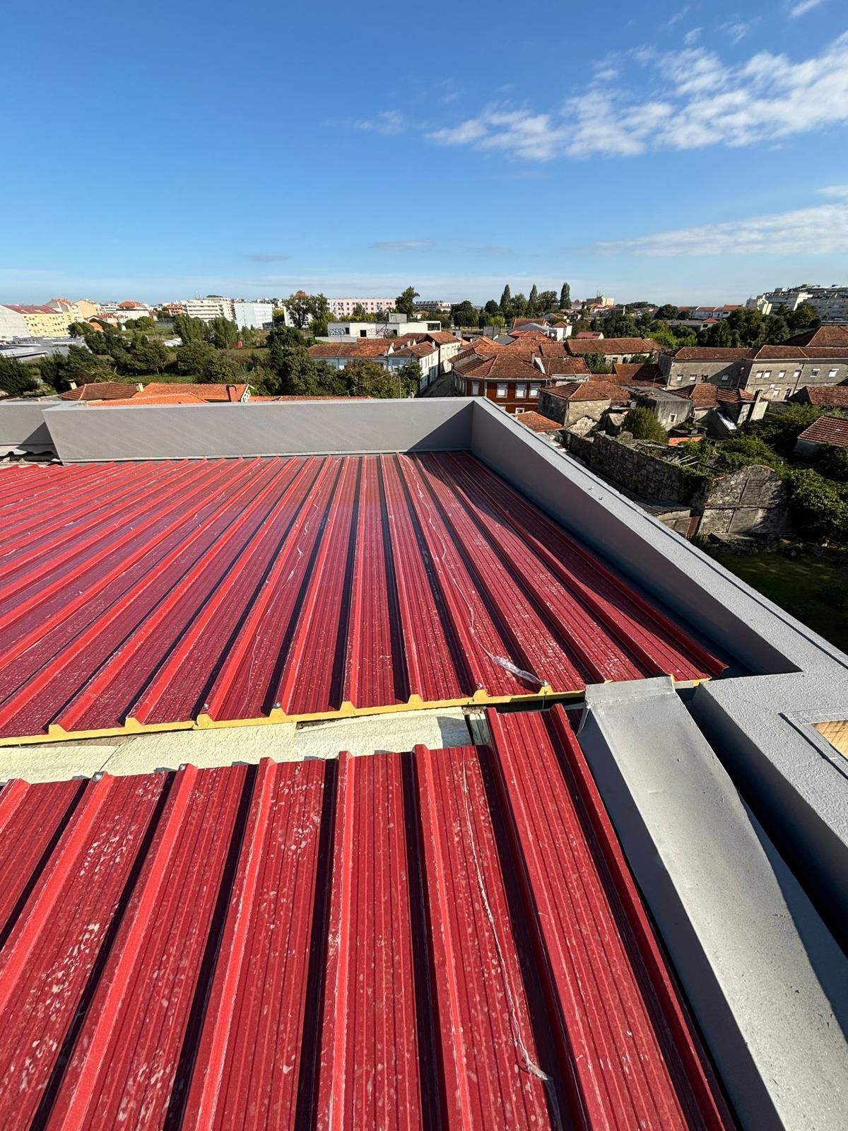 telhado em painel sandwich 5 ondas 30mm RAL3009 vermelho com vista para uma cidade ao fundo.