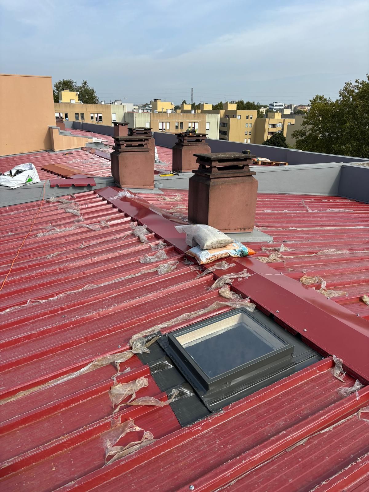 Um telhado em painel sandwich 5 ondas 30mm RAL3009 vermelho com uma claraboia e chaminés.