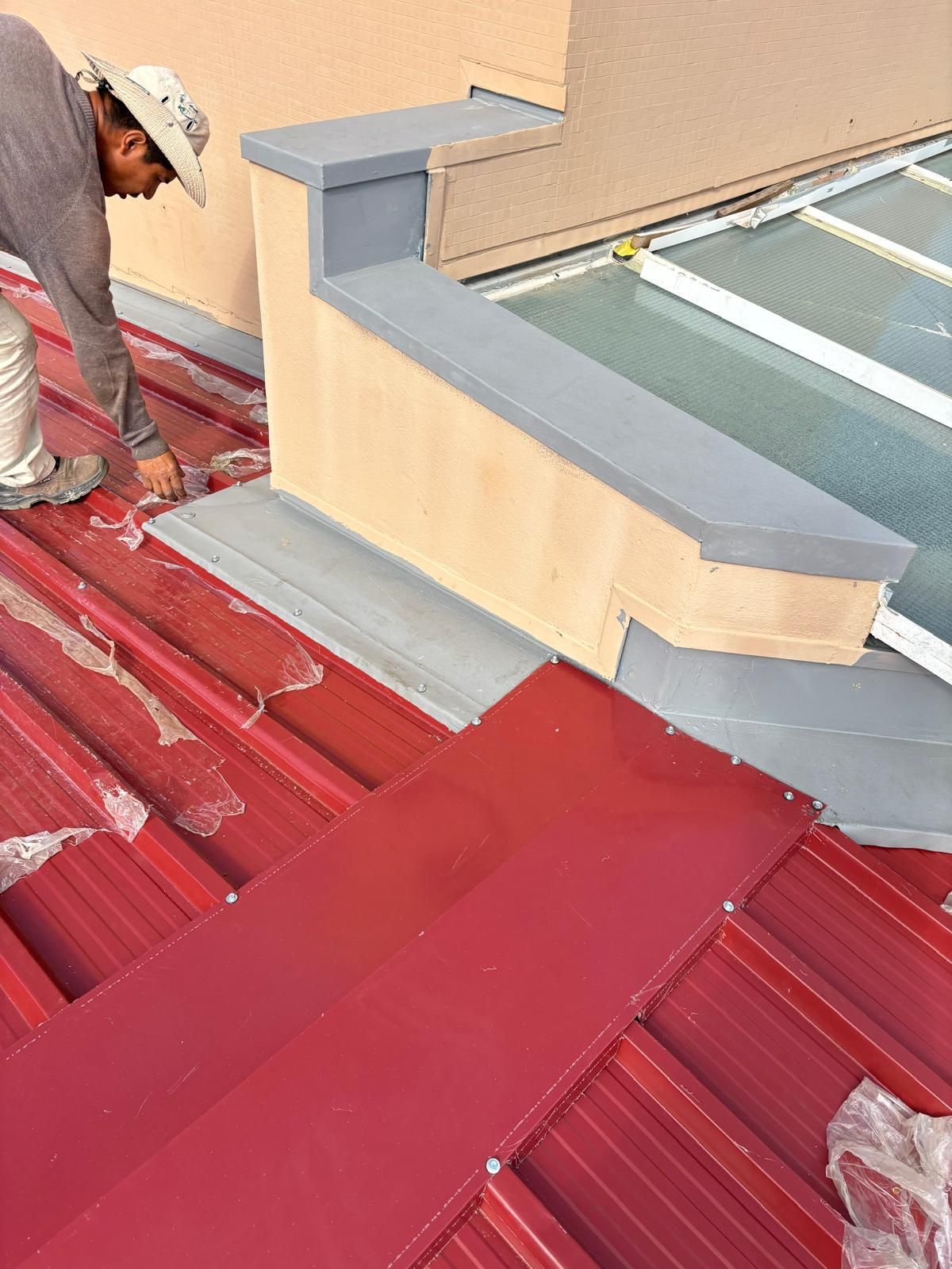 Um homem está trabalhando em um telhado de metal em painel sandwich 5 ondas 30mm RAL3009 vermelho.