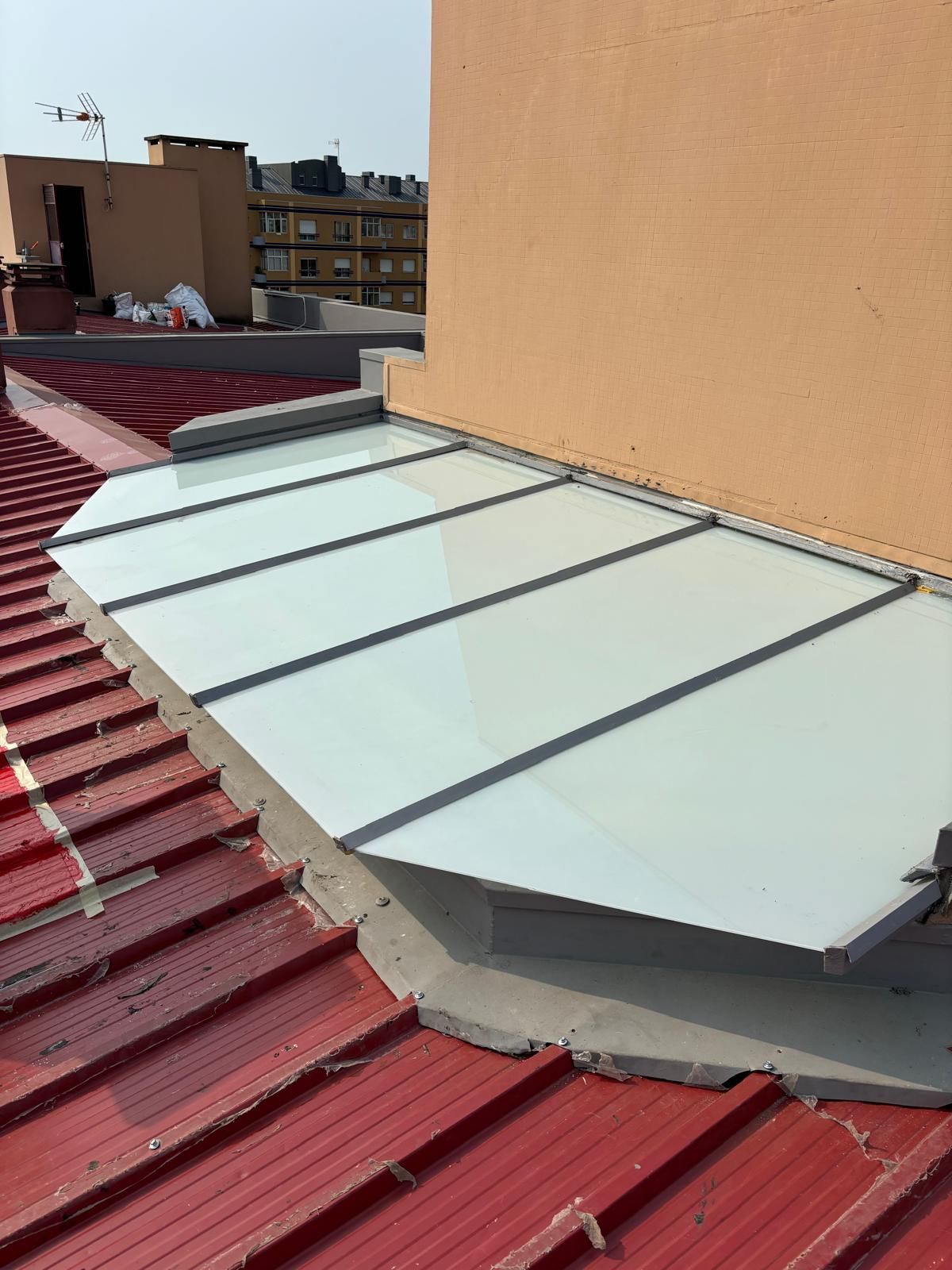 Um telhado vermelho com uma claraboia finalizada com vidros laminados e impermeabilização de estrutura em cinzento no telhado