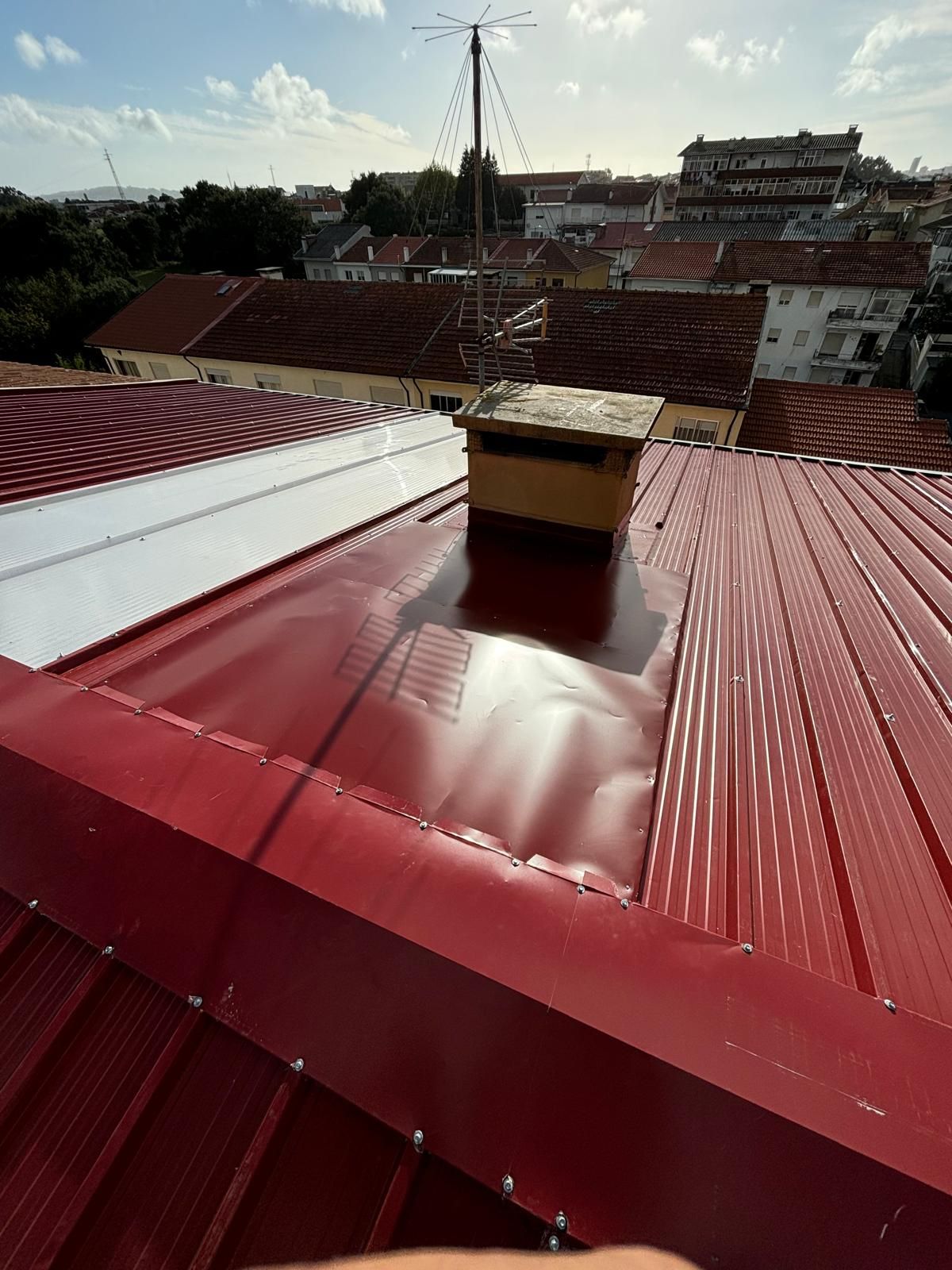 Uma pessoa está em pé no topo de um telhado em painel sandwich 5 ondas 30mm RAL3009 vermelho com uma chaminé.