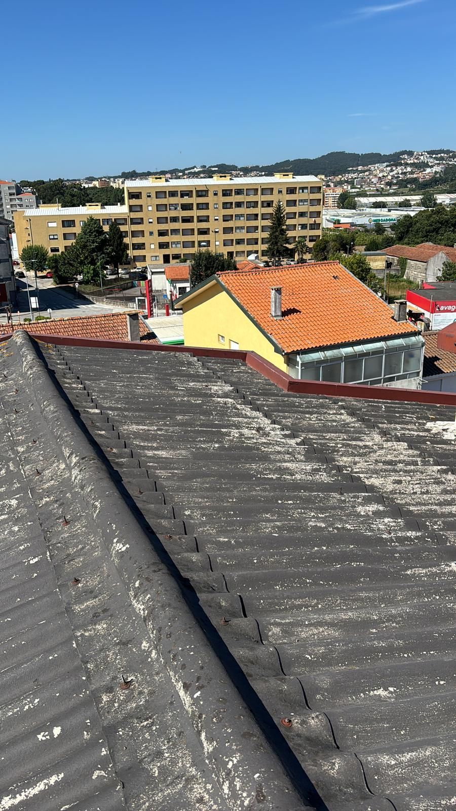 Uma vista do telhado em fibrocimento e amiantode uma cidade com um edifício amarelo ao fundo.