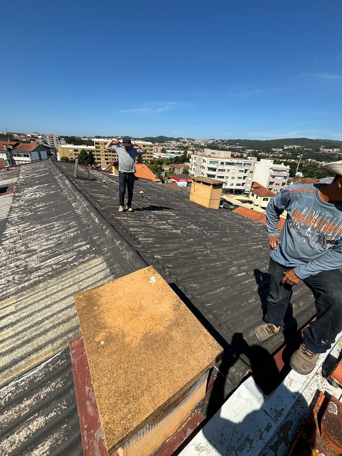Um homem está de pé no telhado de um prédio em fibrocimento e amianto.