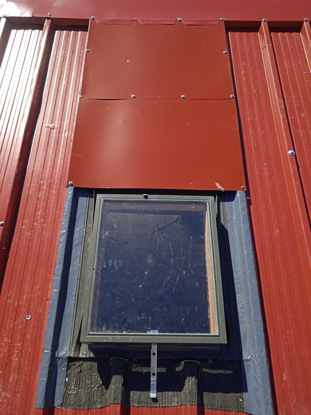 Um telhado vermelho com uma claraboia em cima e um rufo superior à cor.