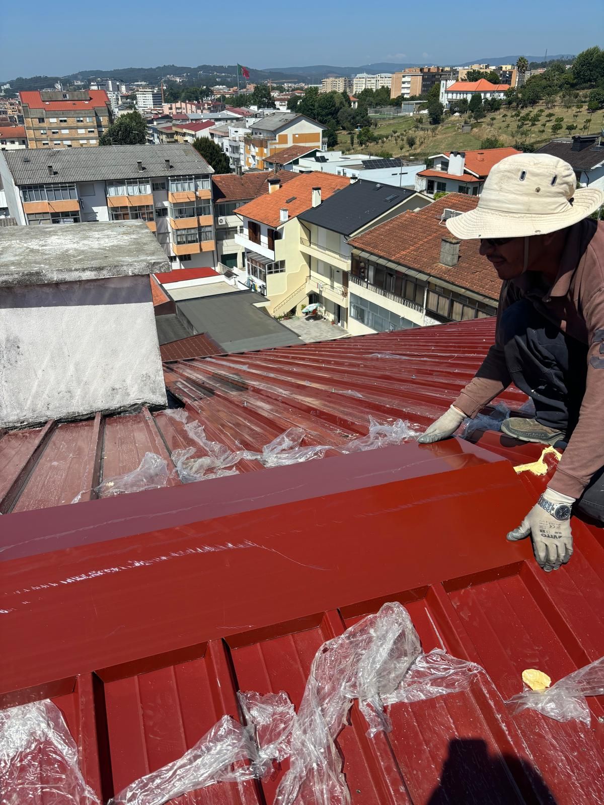 Um homem está pintando um telhado em painel sandwich 5 ondas 30mmcom uma cidade ao fundo