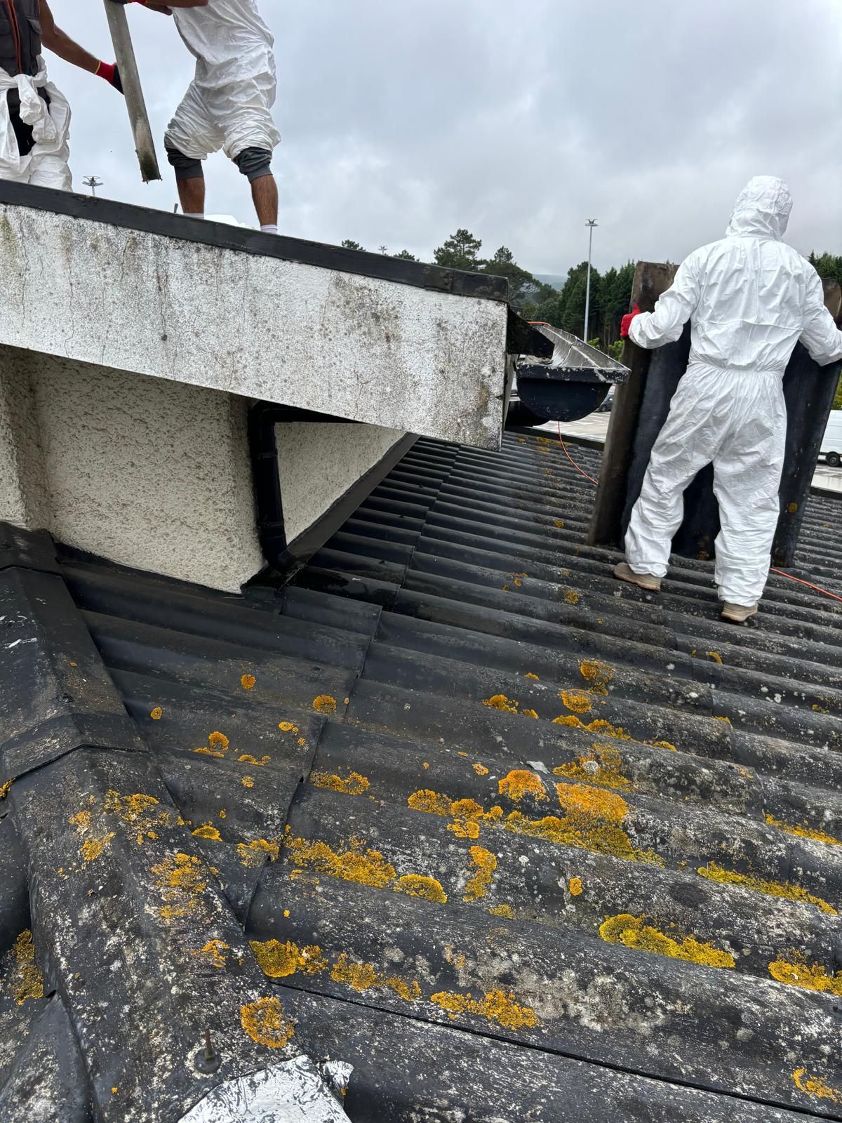 Dois homens de fato tyvek branco proteção de amianto estão trabalhando no telhado de um prédio.