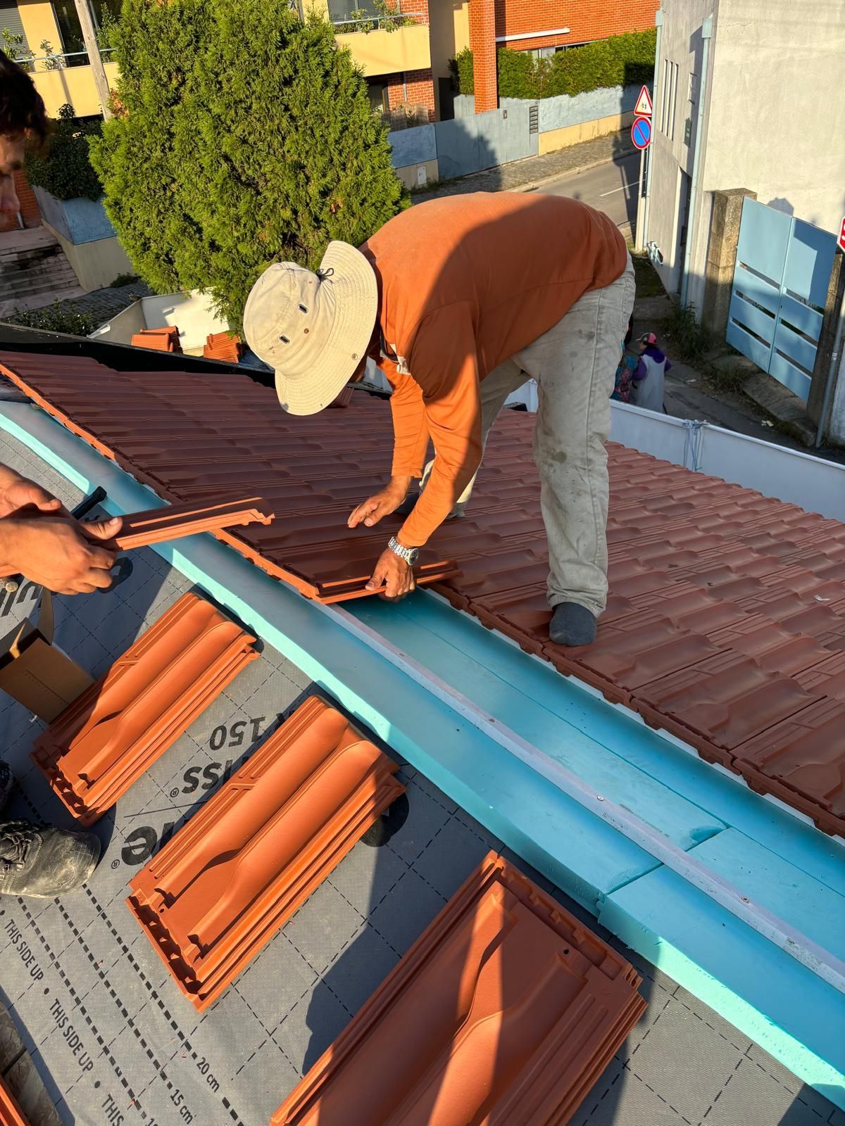 Um homem usando um chapéu está trabalhando em um telhado de telhas cerâmicas laranjas