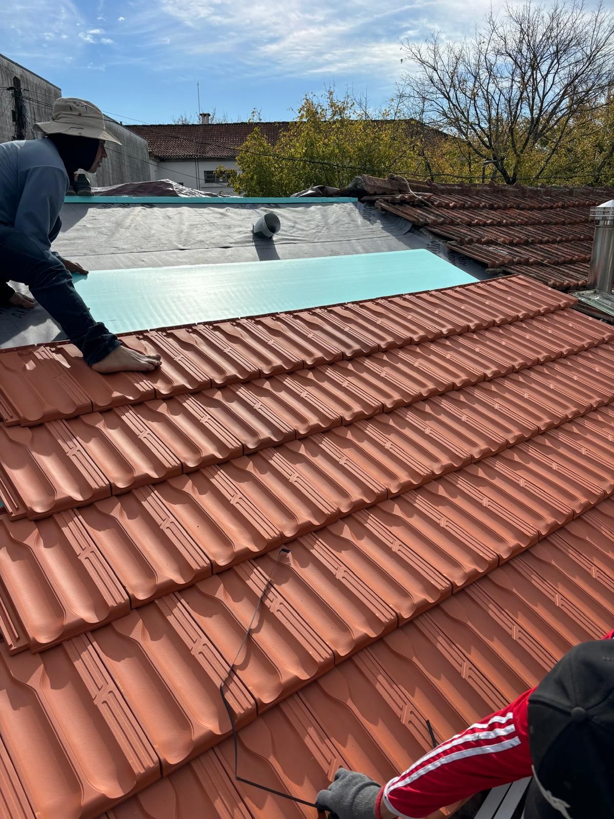 Um homem está trabalhando no telhado de uma casa telhas cerâmicas laranjas.