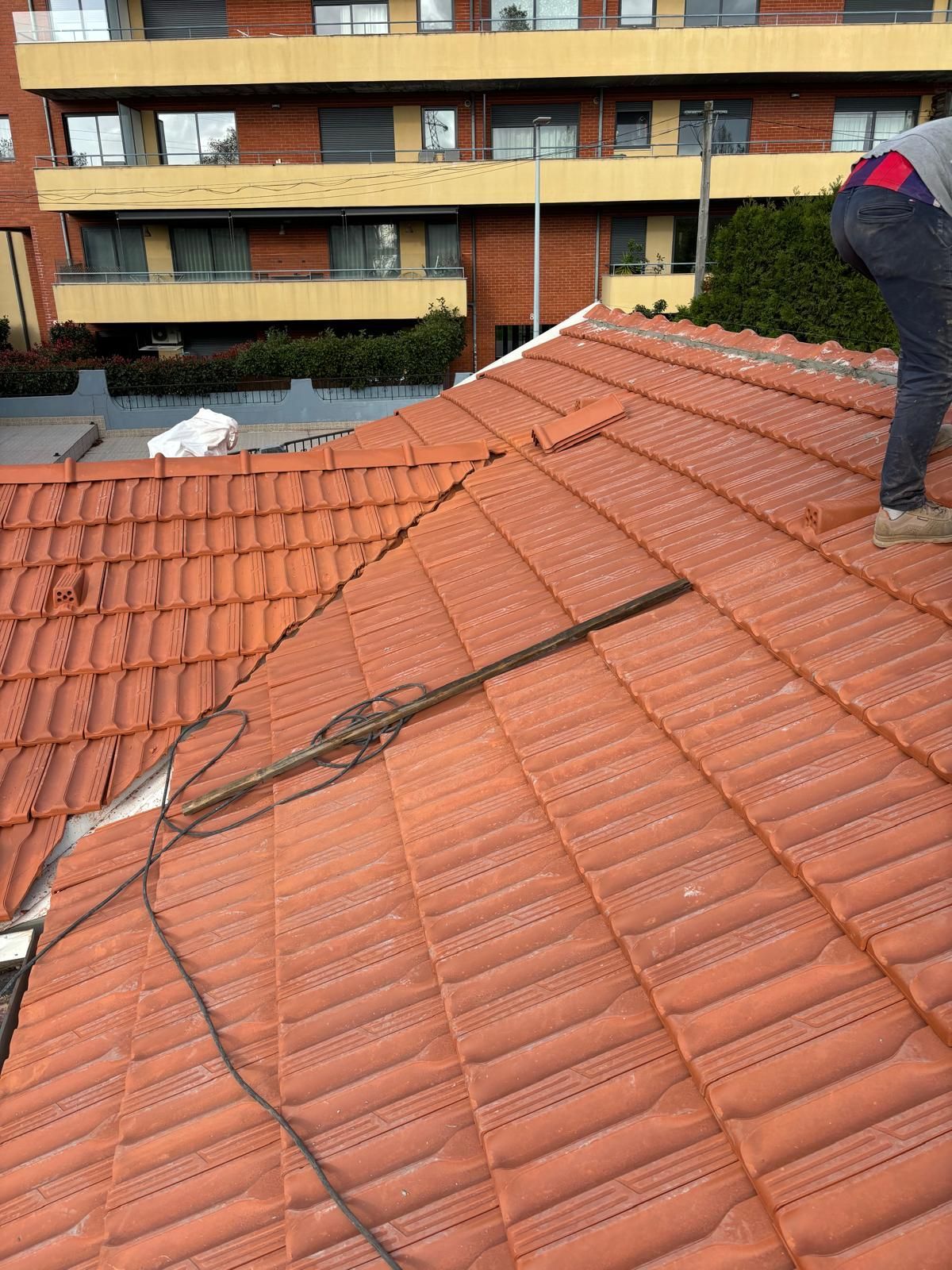 Um homem está de pé no topo de um telhado de telhas cerâmicas laranjas.