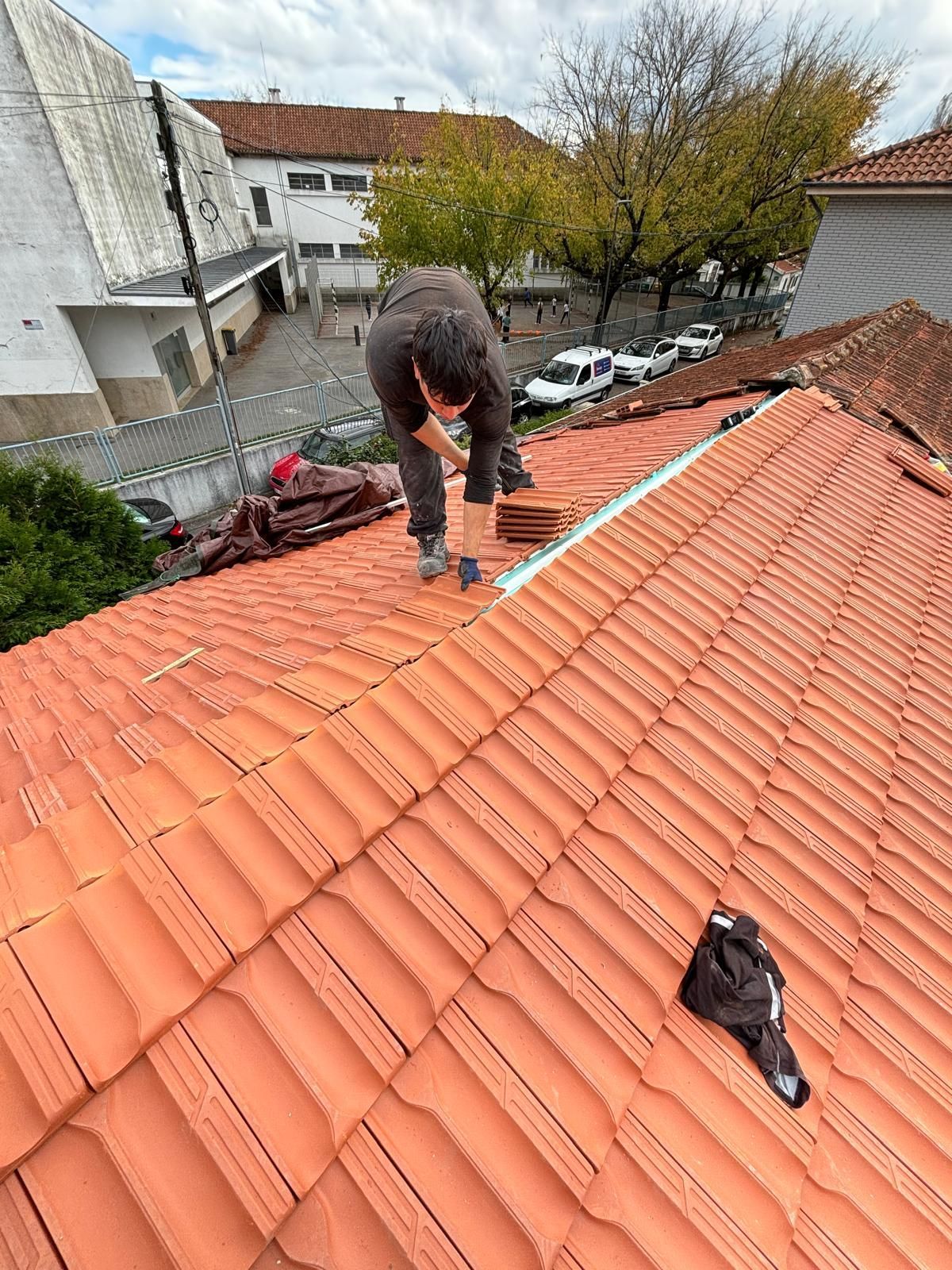 Um homem está em pé no topo de um telhado de telhas cerâmicas laranjas