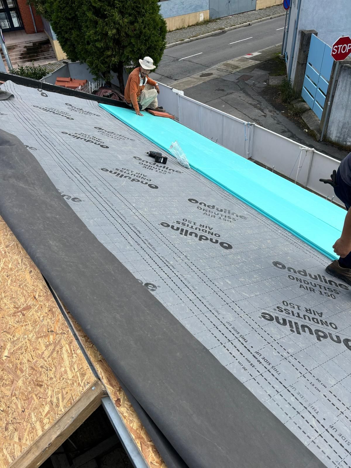 Um homem está trabalhando em um telhado com uma placa de pare ao fundo