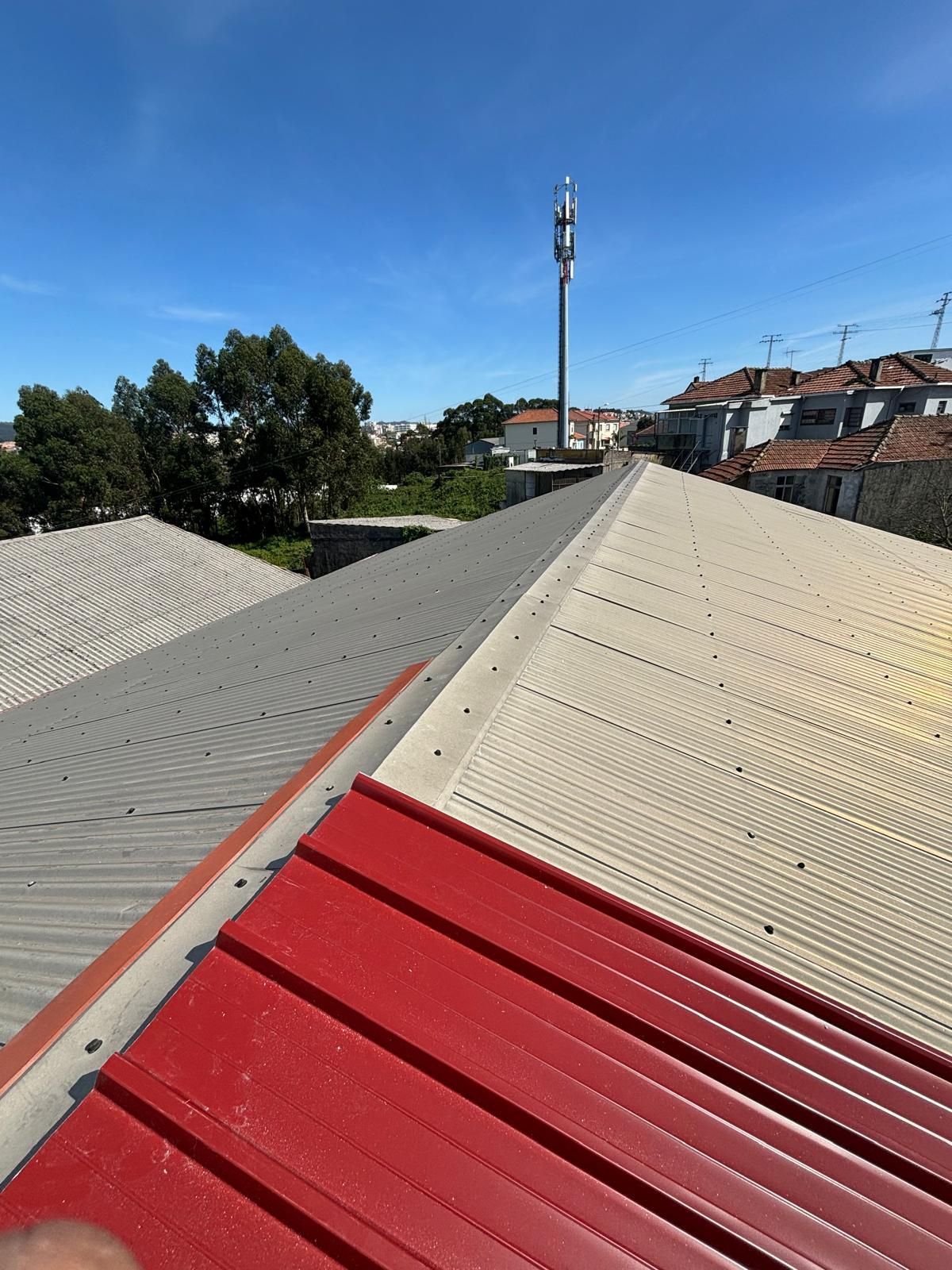 Um telhado em painel sandwich 5 ondas 30mmvermelho e branco com uma torre de celular ao fundo.