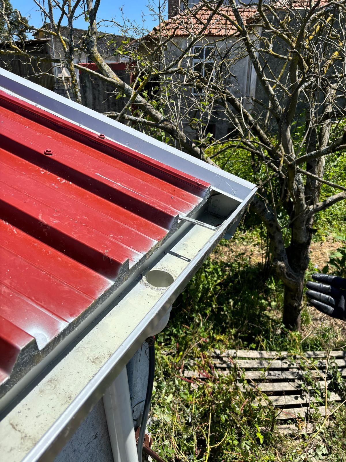 Uma pessoa está limpando uma calha em um telhado vermelho.