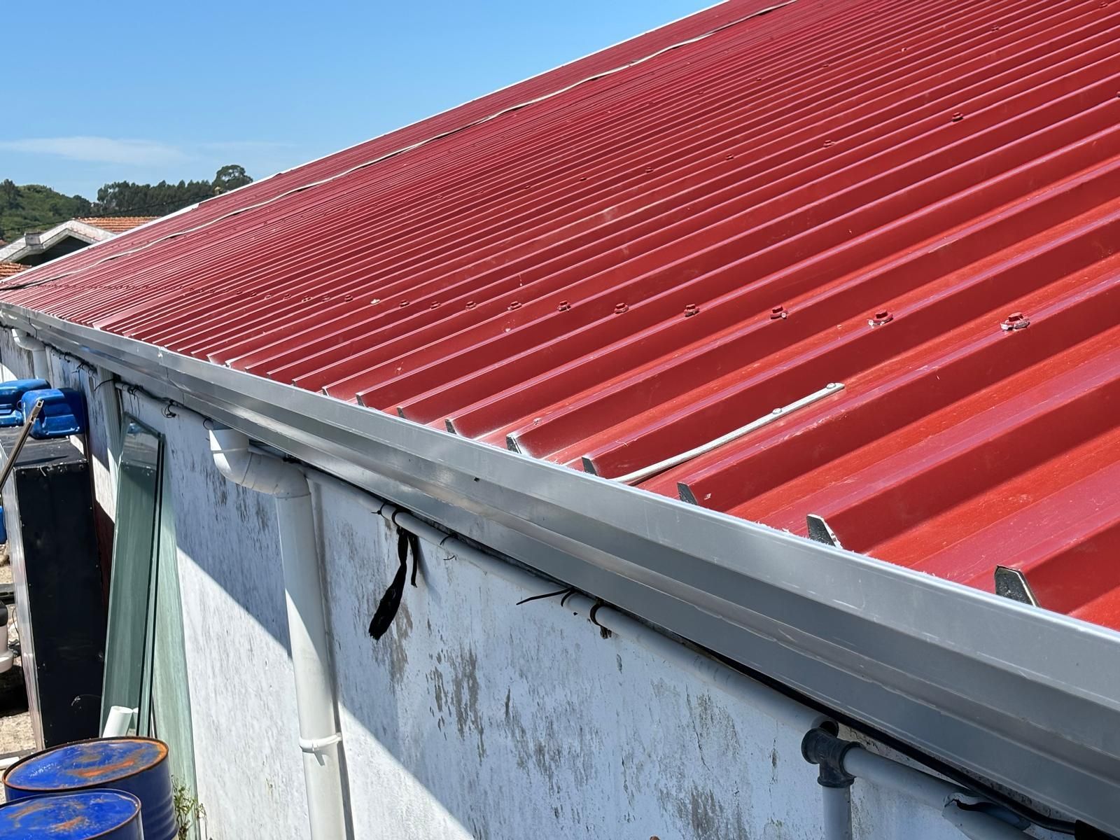Um telhado vermelho com uma calha branca na lateral de um prédio.