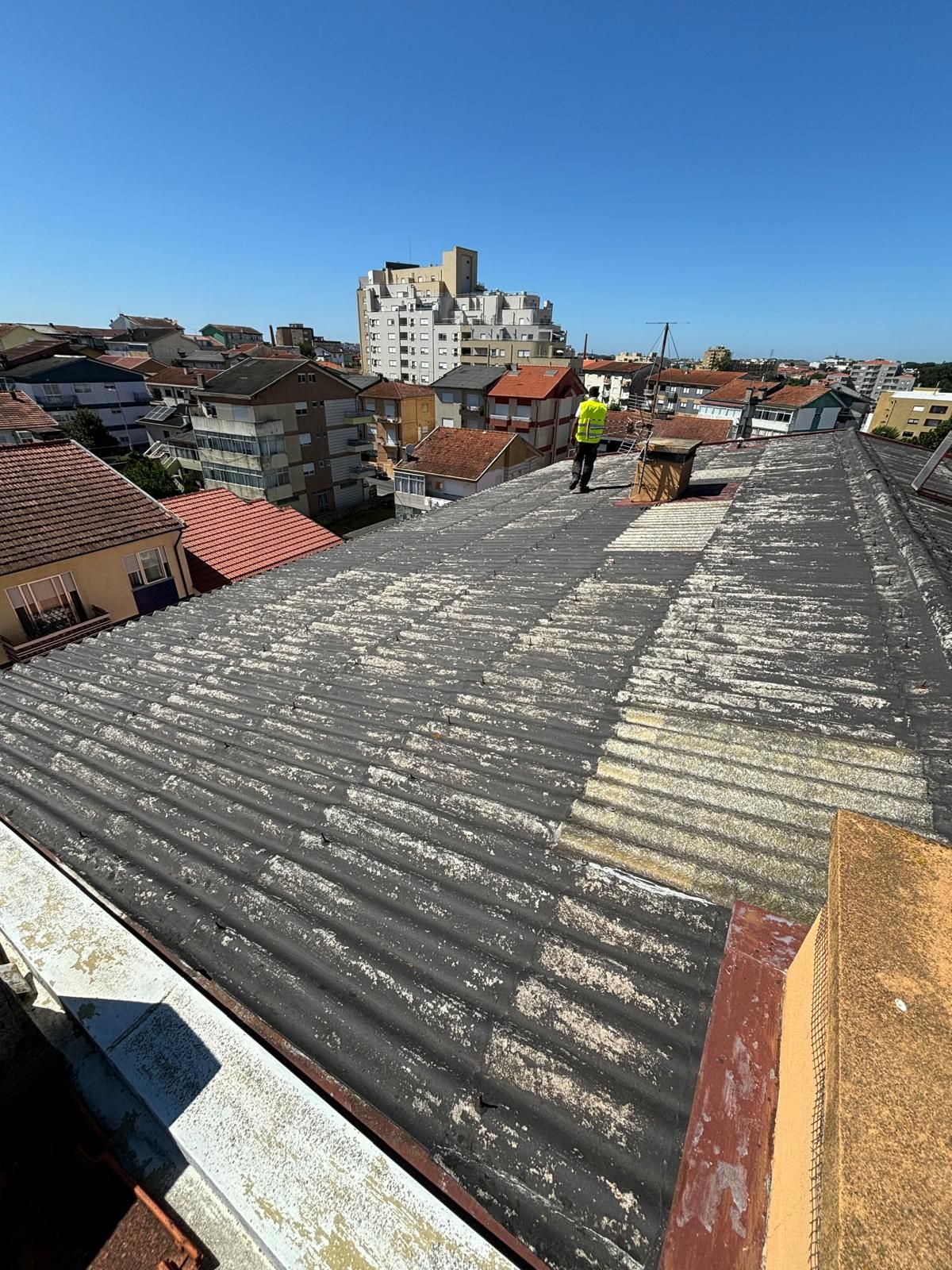 Um homem está de pé no telhado em fibrocimento e amianto de um prédio.