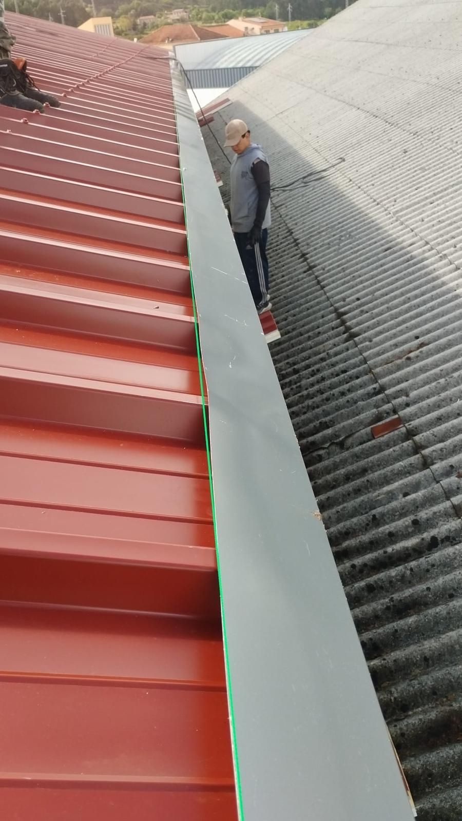 Um homem está de pé em um telhado em painel sandwich 5 ondas 30mm próximo a uma calha.