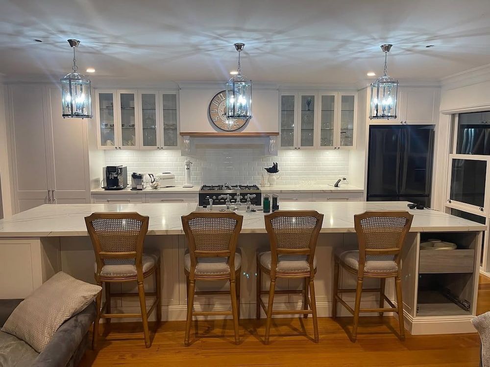 A Kitchen With White Cabinets a Stove a Clock on the Wall and Stools — Canberra Bathroom Solutions in Tuggeranong, ACT