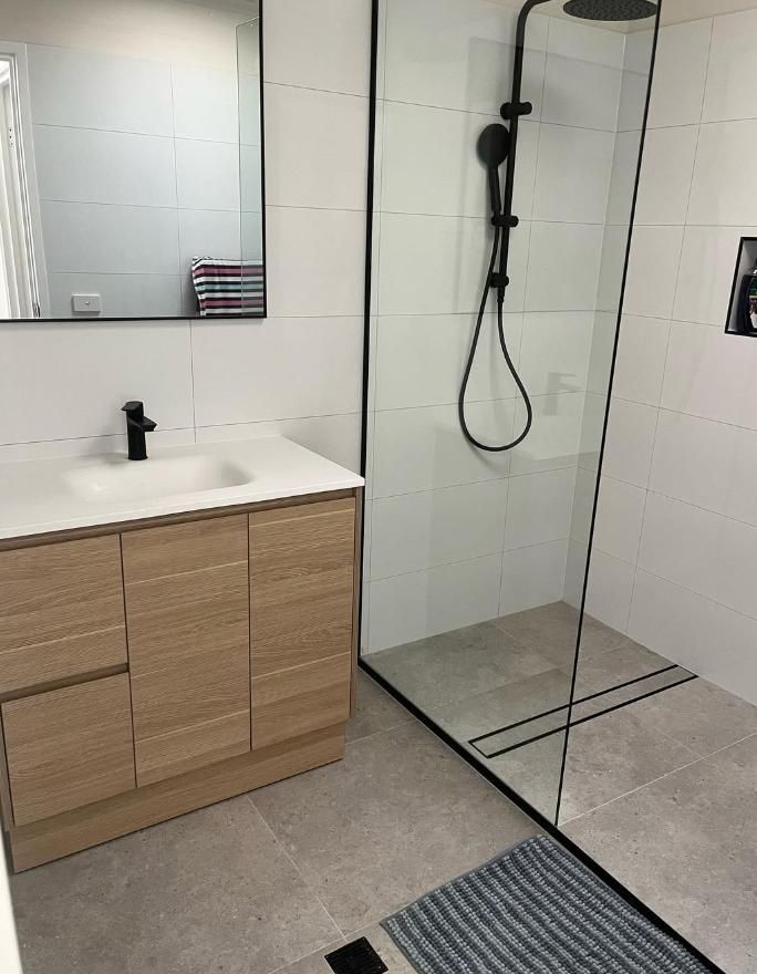 Modern Bathroom With Light Wood Vanity, Black Fixtures, Walk-in Shower With A Glass Door, And White Tiled Walls — Canberra Bathroom Solutions in Ngunnawal, ACT