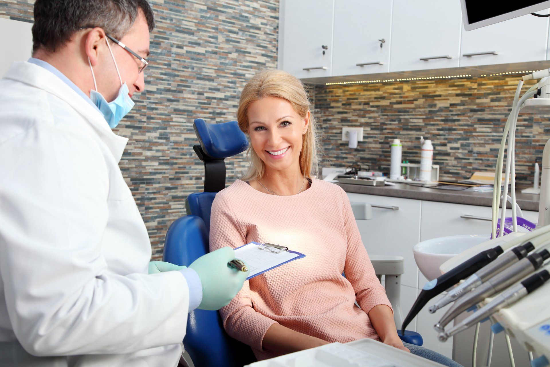 Dentist with white lab coat looks at smiling blonde female patient