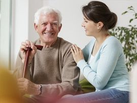 older man with cane sitting beside caregiver at home