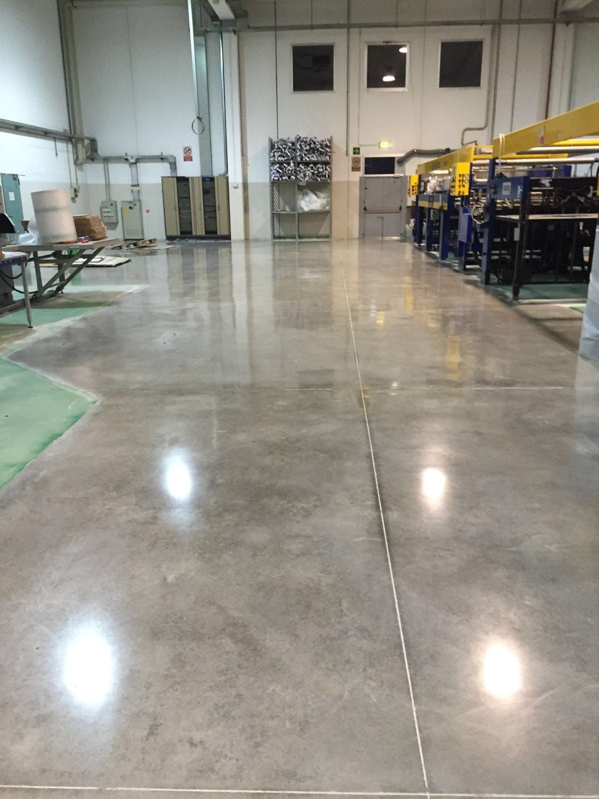 Pavimento in cemento lucidato in un ambiente industriale, che riflette le luci provenienti dall'alto.