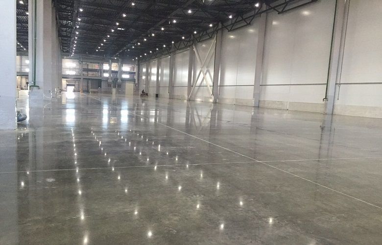 Grande magazzino vuoto, con pavimento in cemento lucidato, illuminato da luci soffuse.