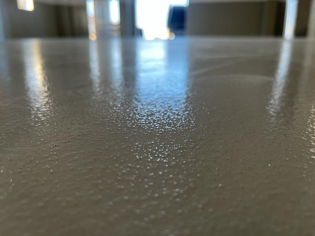 Primo piano di un pavimento grigio chiaro lucido con una trama punteggiata che riflette la luce.